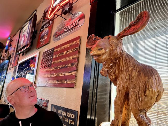 Man gazing admiringly at a wooden moose sculpture